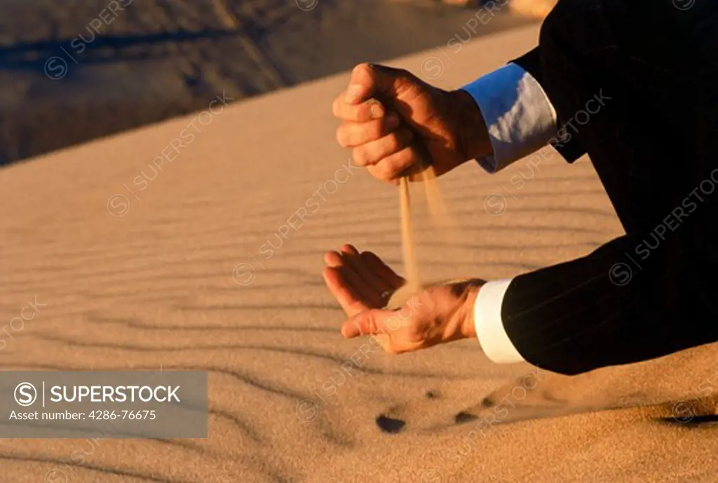 Man in business suit pouring desert sand through his hands