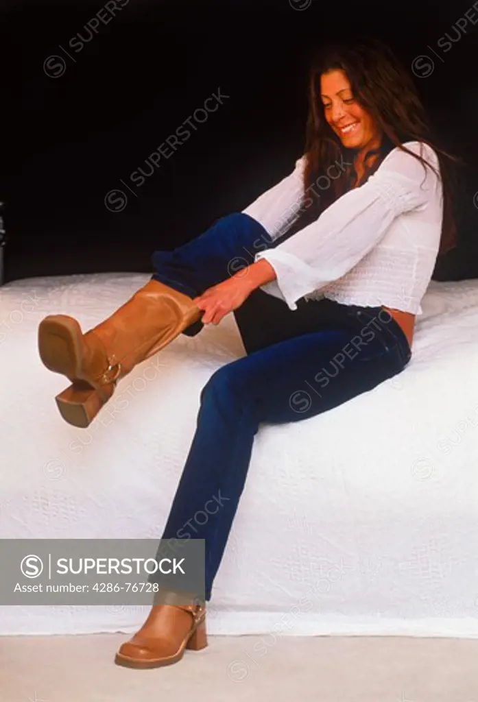 Woman in bedroom pulling on pair of leather boots