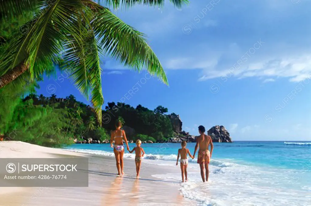 Family of four walking along sandy shore on La Digue Island holiday in Seychelles