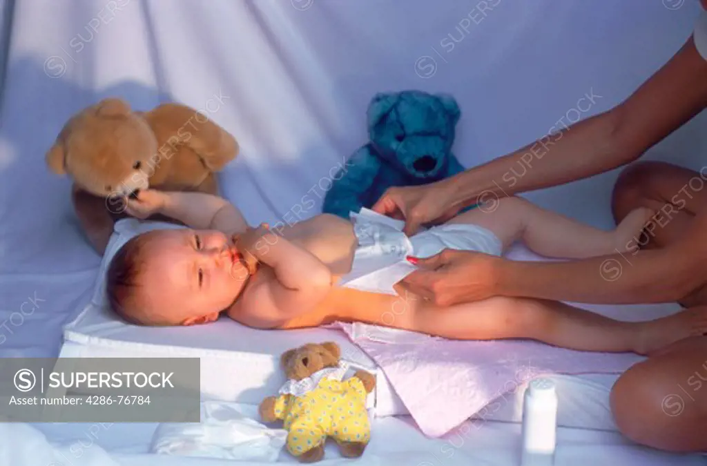 Mother changing babies diaper in bedroom morning light at home
