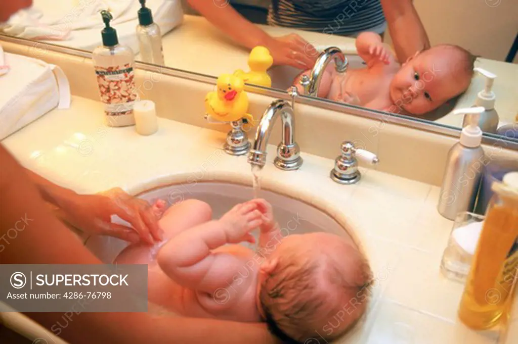 Mom bathing baby 3-6 months old in bathroom sink