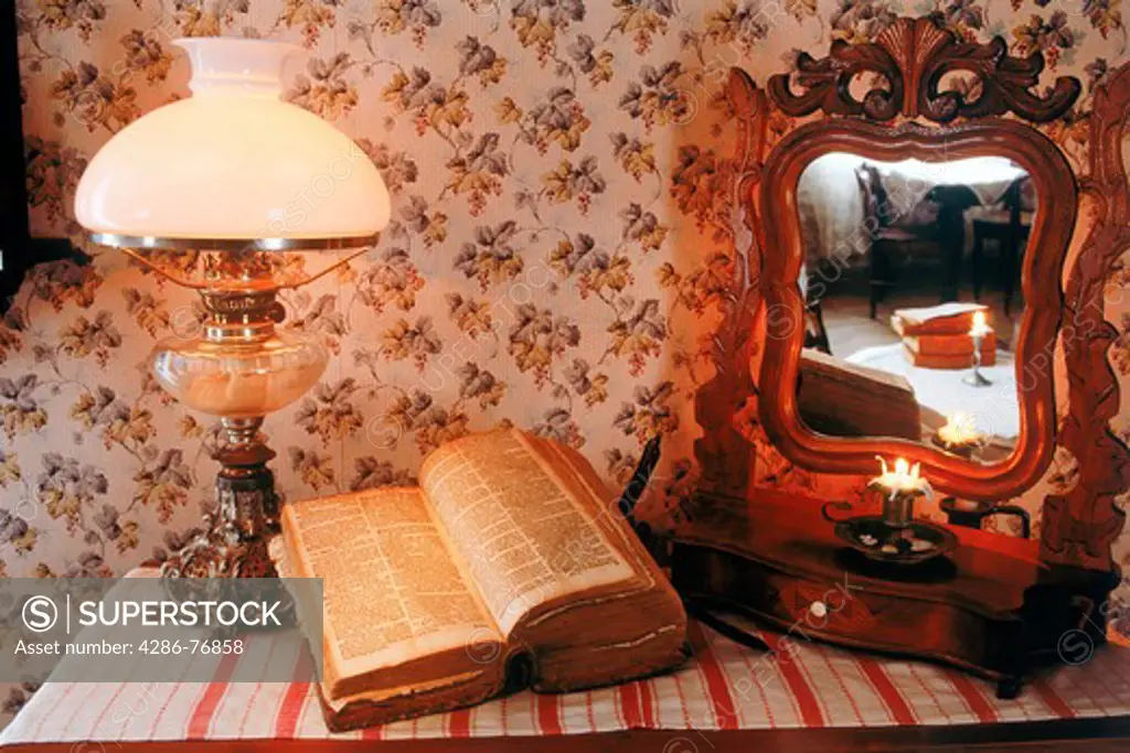 Antique wooden bureau with Bible, lamplight and mirror reflecting candle and old bedroom interior in Sweden