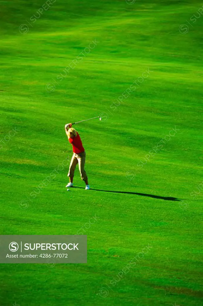 Woman with perfect form hitting iron shot off lush green fairway