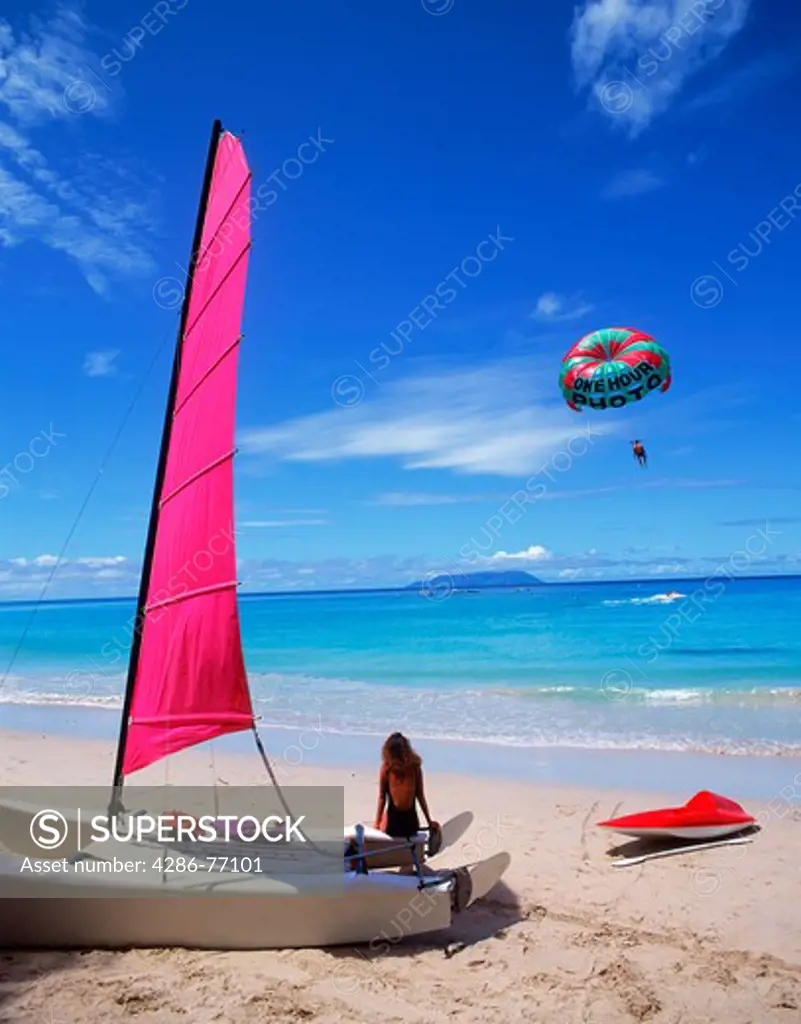 Woman sitting on catamaran on beach watching wind sailing on Mahe Island in the Seychelles