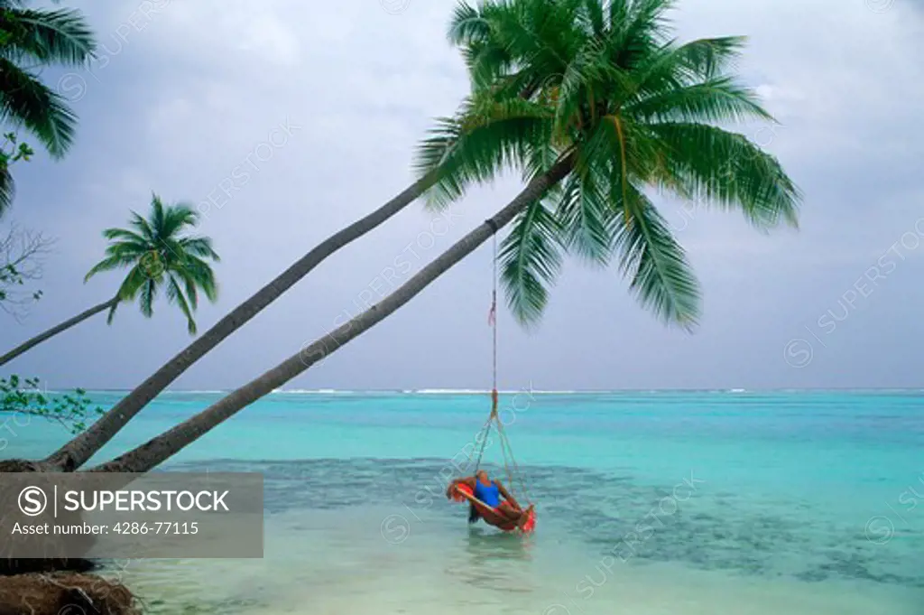 Woman relaxing in swing over aqua waters under palm trees on Meeru Island in the Maldives
