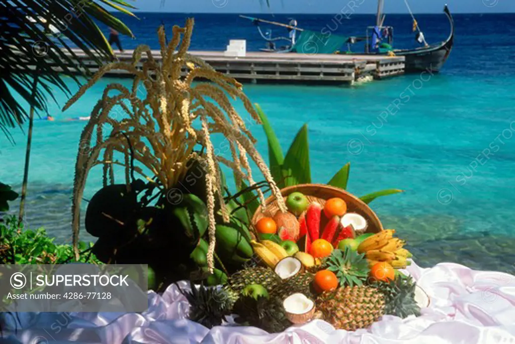 Baskets of fresh fruits including coconut, pineapple, papaya, guava and apples next to harbor on Fihalhohi Island in Maldives