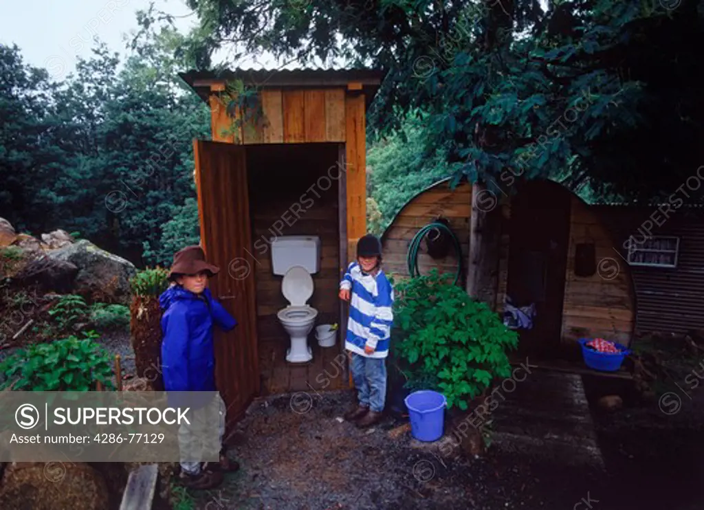 Kids standing next to old family wooden dunny or outhouse in country home backyard in Tasmania