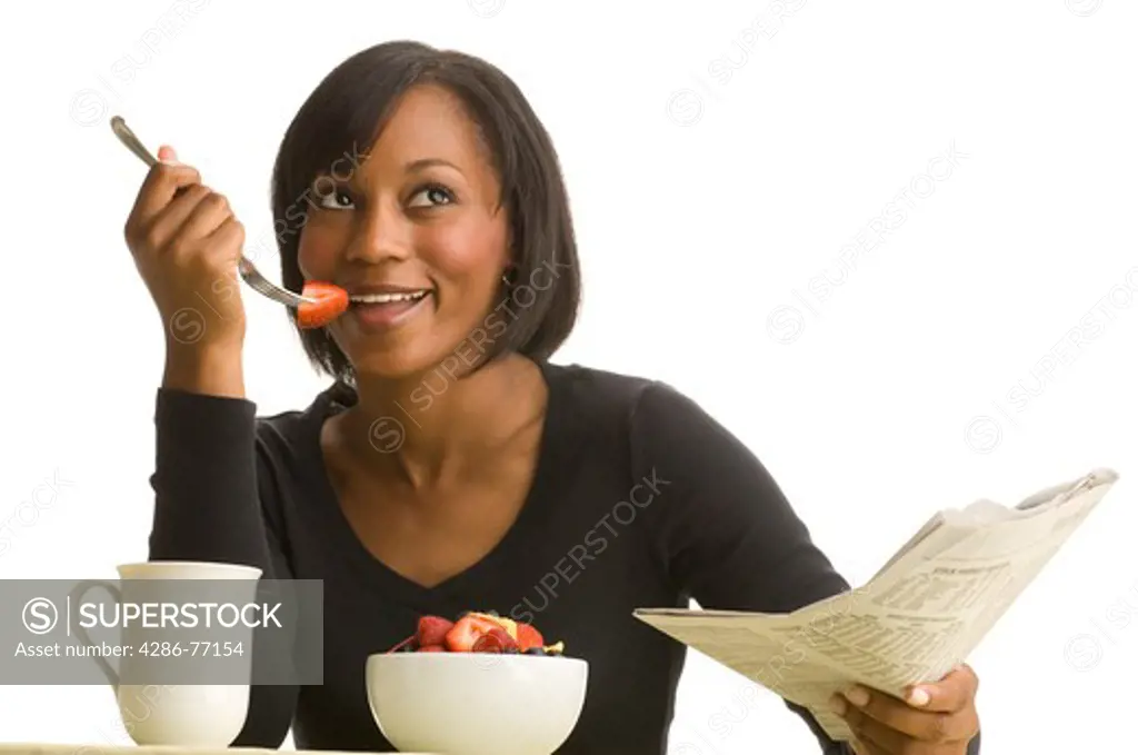 Studio portrait of young African American woman enjoying healthy breakfast and reading newspaper