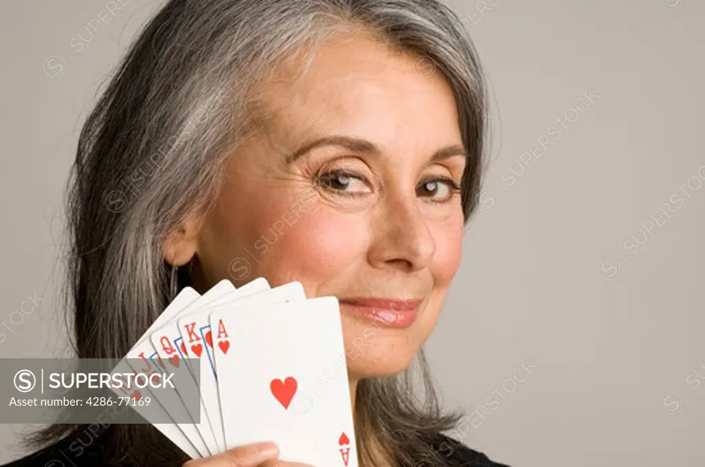 Studio shot of mature woman holding up a royal flush in cards