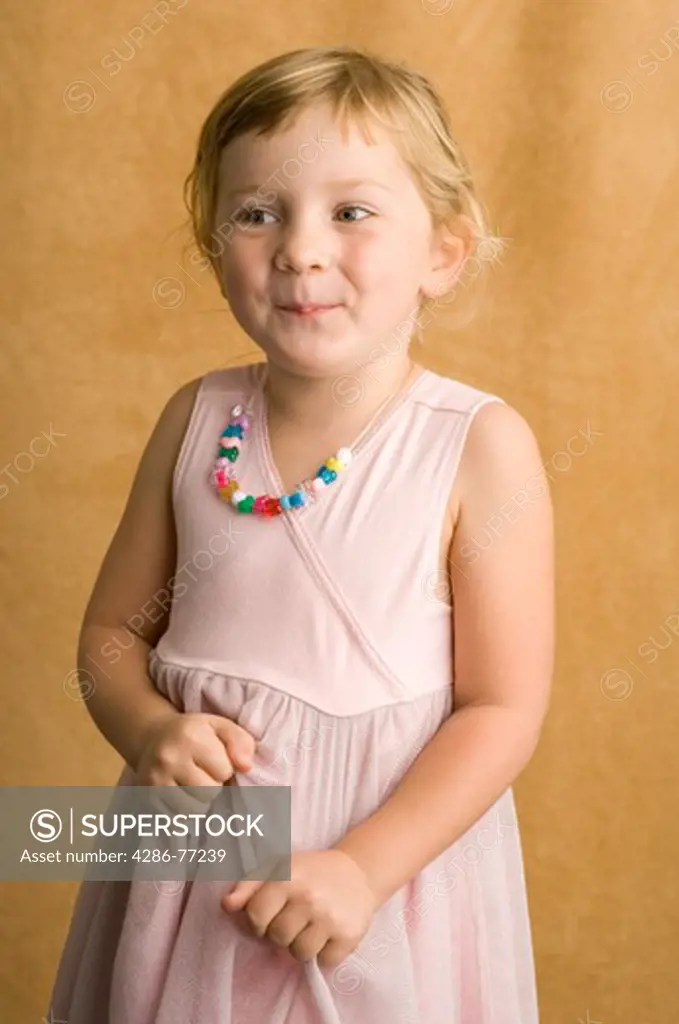 Studio portrait of young blond girl in pink dress, tan backdrop