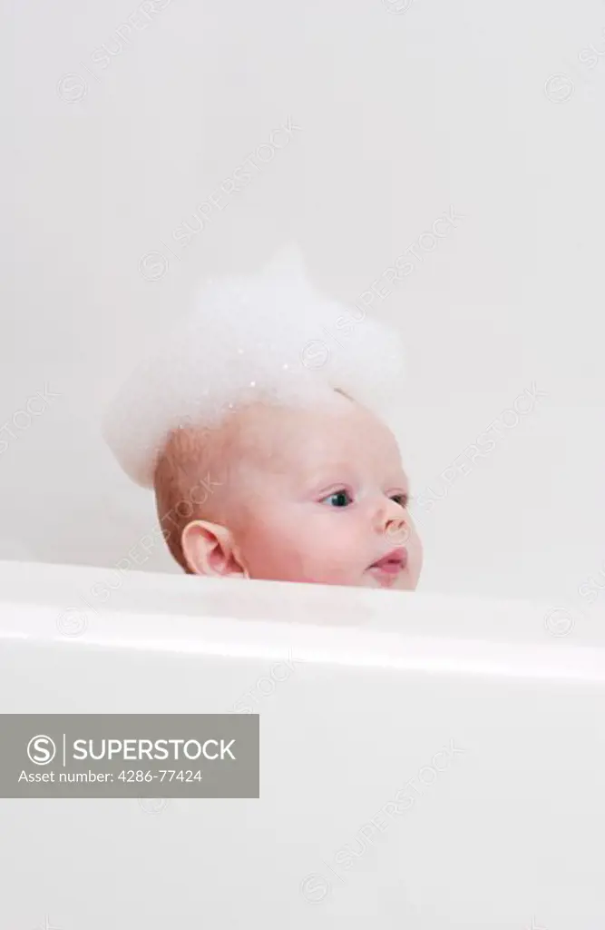 Baby in bath tub with bubbles on head