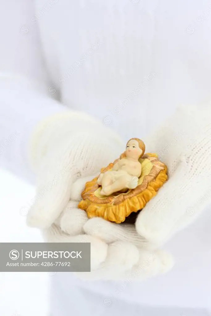 Hands with winter gloves holding Baby Jesus nativity scene figure