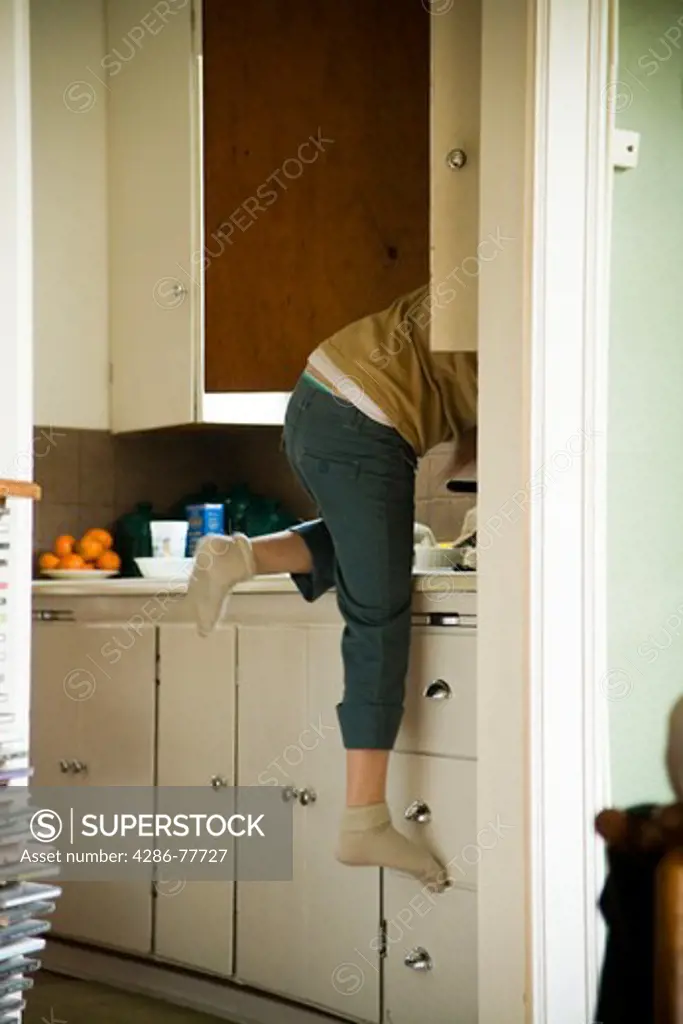 Back side of a woman climbing on the kitchen counter