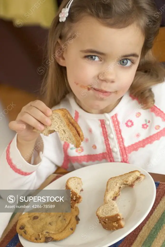 Young child with a half eaten peanut butter jelly sandwich and a chocolate chip cookie on a plate.