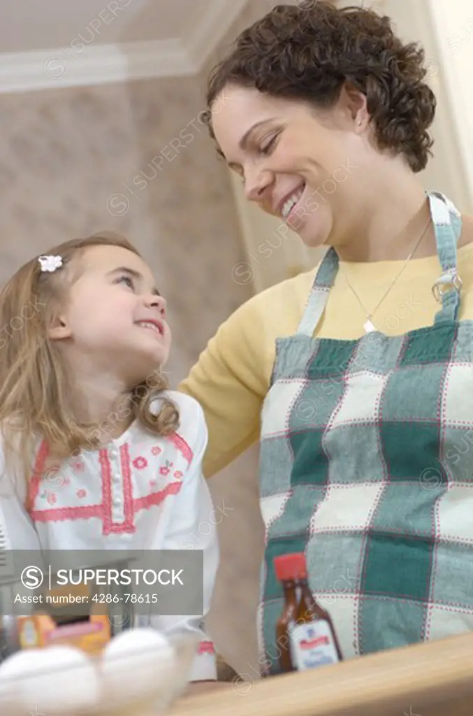 A low angle view of a pregnant mother smiling down at her young daughter as they bake together in the kitchen.