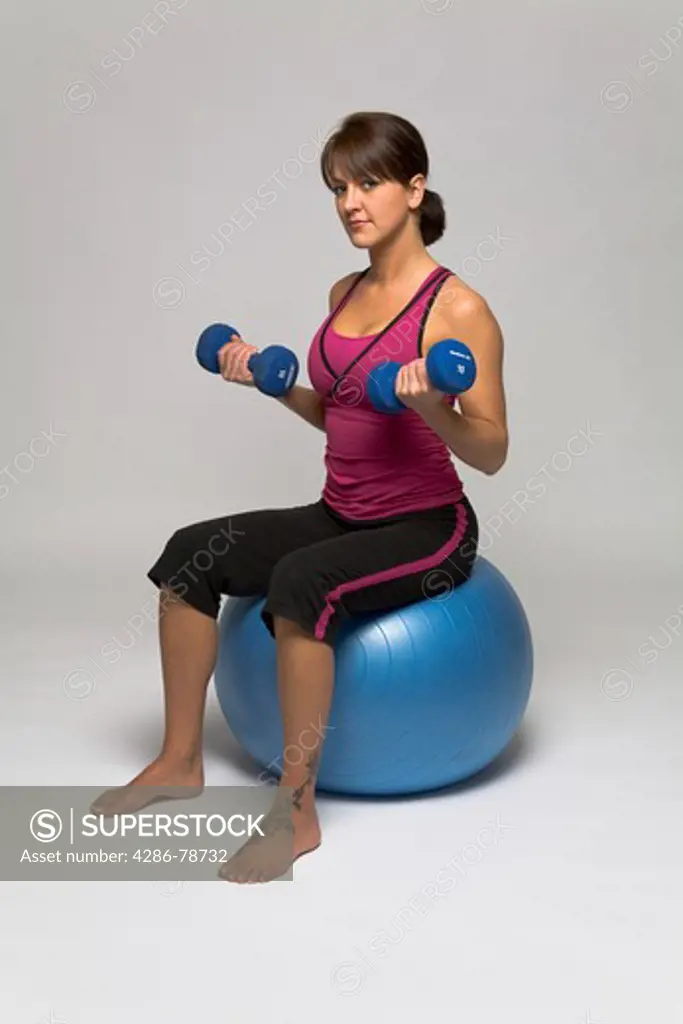 Woman sitting on a fitness ball doing a double bicep dumbell curl