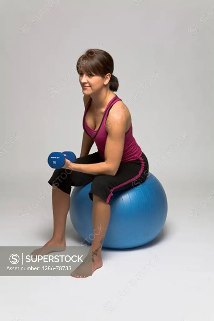 Woman sitting on a fitness ball doing a single bicep dumbell curl