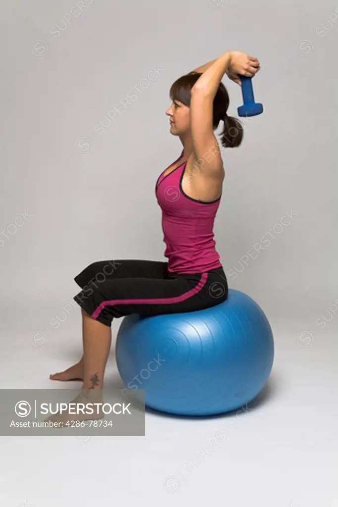 Woman sitting on a fitness ball doing an overhead dumbell tricep extension