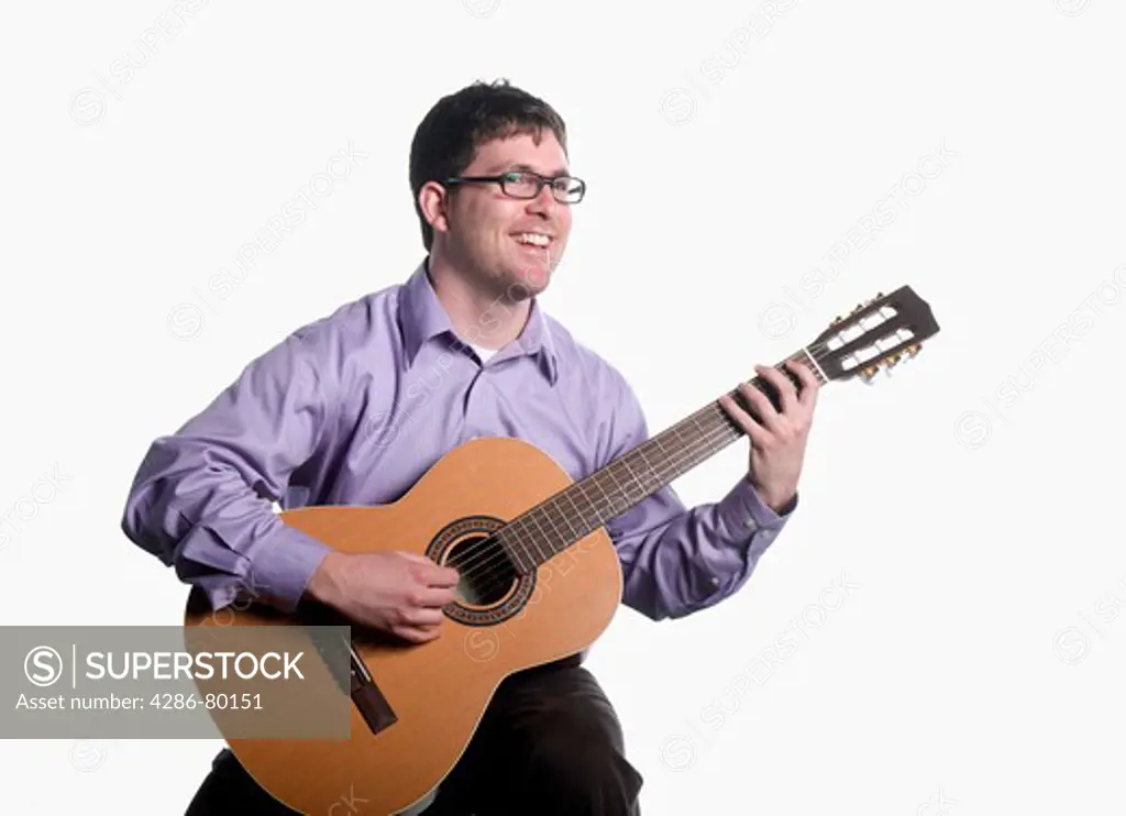 A college age man holds and plays a classical guitar. 