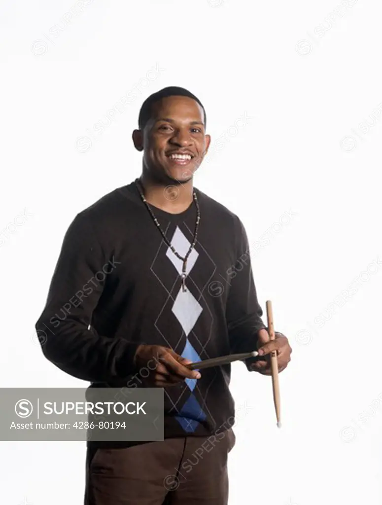 A college age man holds his drum sticks and smiles. 