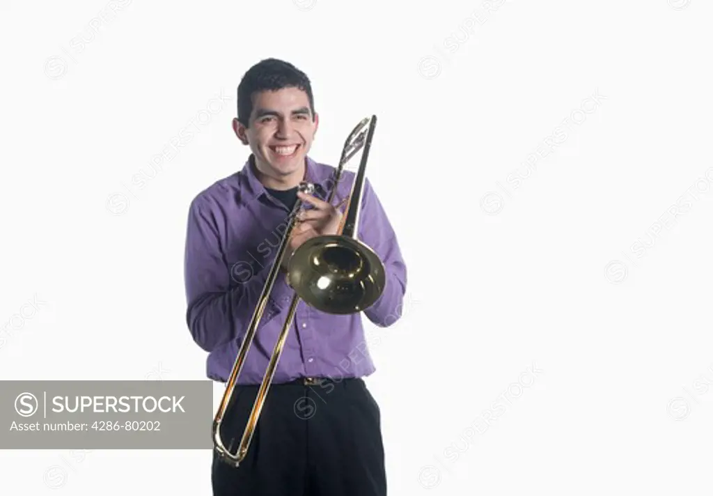 A college age man holds his trombone and smiles.