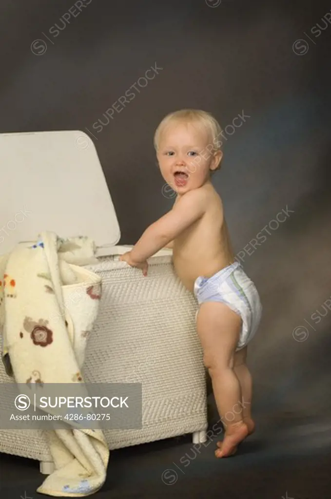 Portrait of a toddler in diapers playing in the hamper