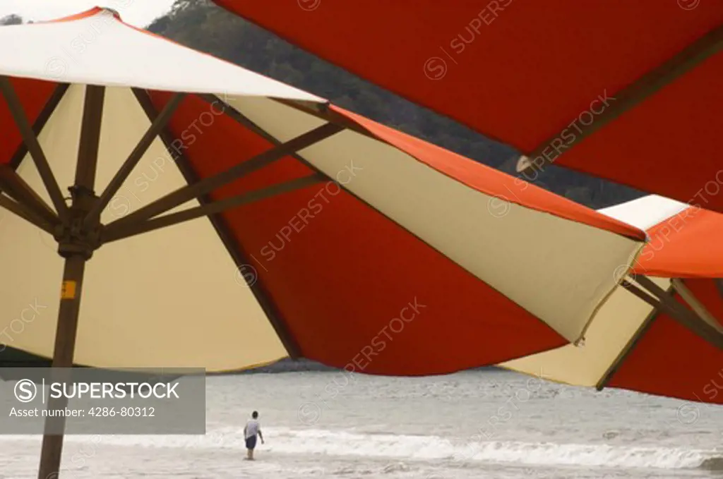 Close up of beach umbrellas with a lone man by the shore in La Manzanilla