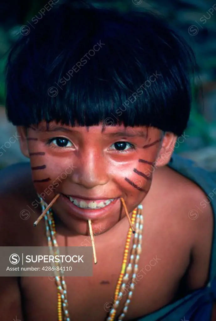 Portrait of smiling Yanomam boy with painted face and sticks projecting from holes perforated around his mouth, Brazil and Venezuela.