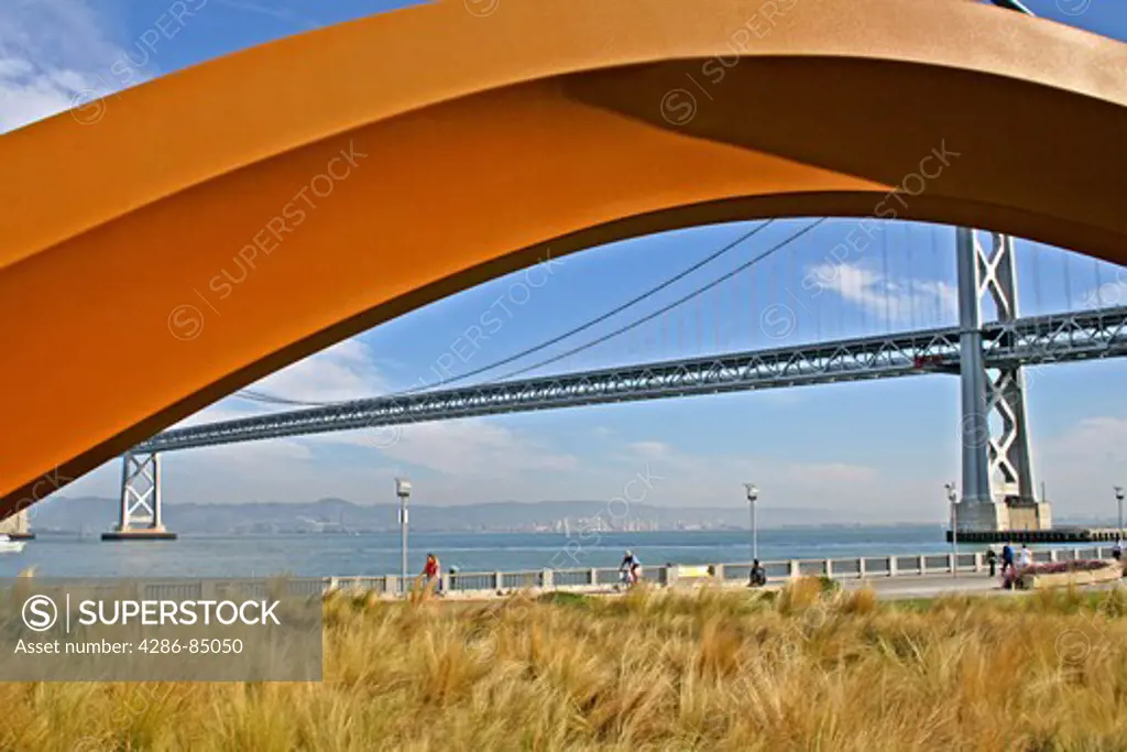 Bay Bridge framed by red arch of Embarcadero area public art sculpture San Francisco California