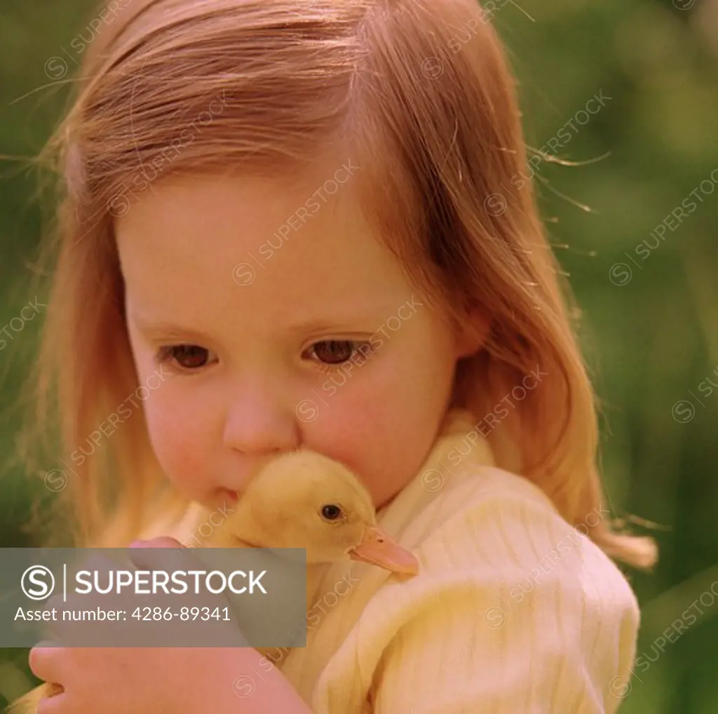 Close-up of a young girl with red hair holding a duckling