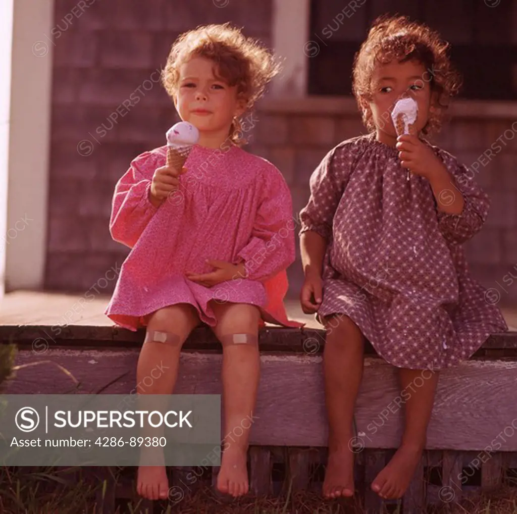 Two young ethnically diverse girls sitting on the steps eating ice cream cones