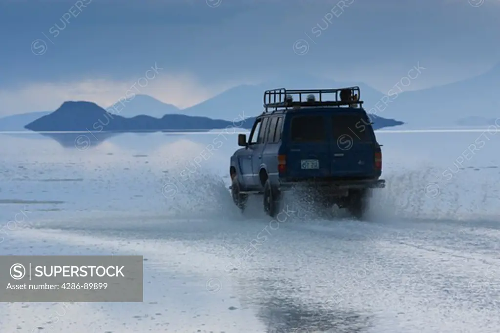 Travelers drive their SUV across a the Salar de Uyuni, a flooded salt flat,  in Bolivia