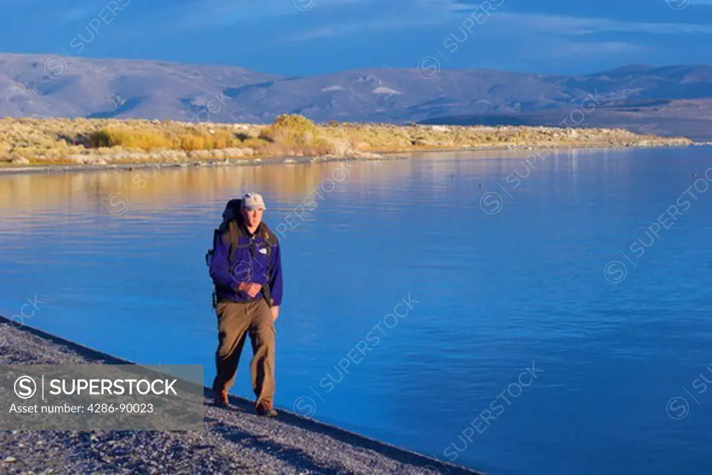 Man with backpack hiking along shore of Mono Lake, CA at sunrise