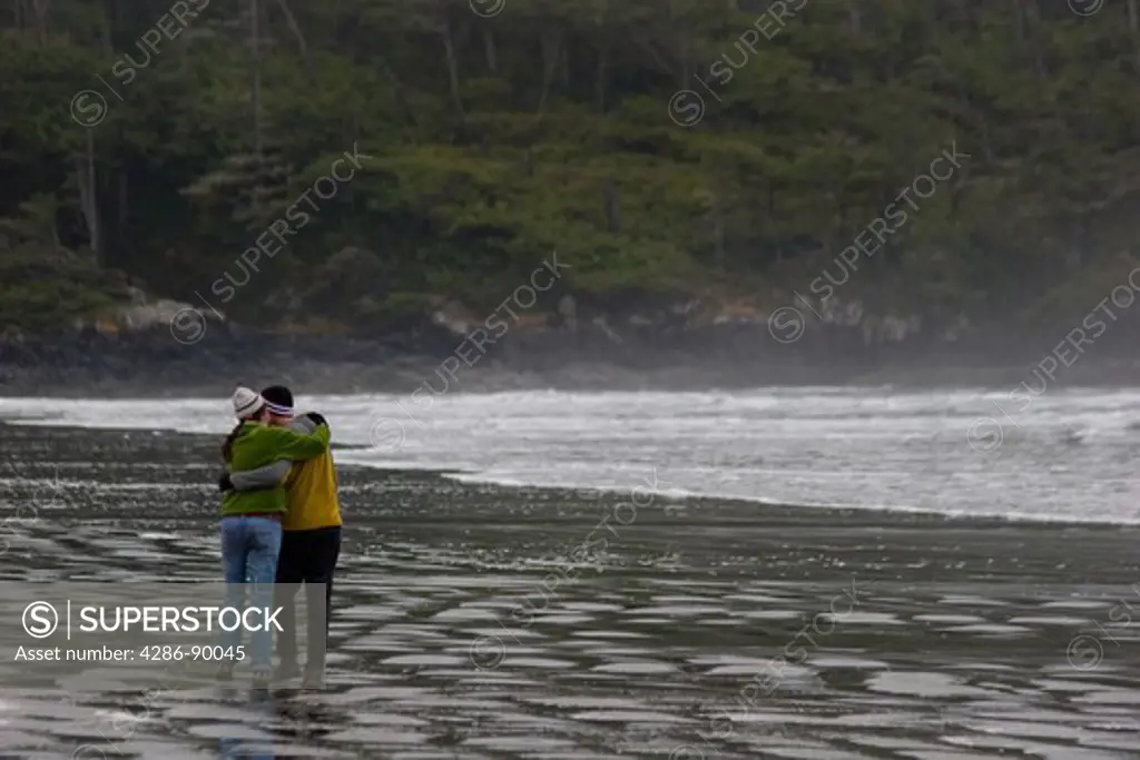 Man and woman walking along the beach sharing a tender moment, near Tofino, BC