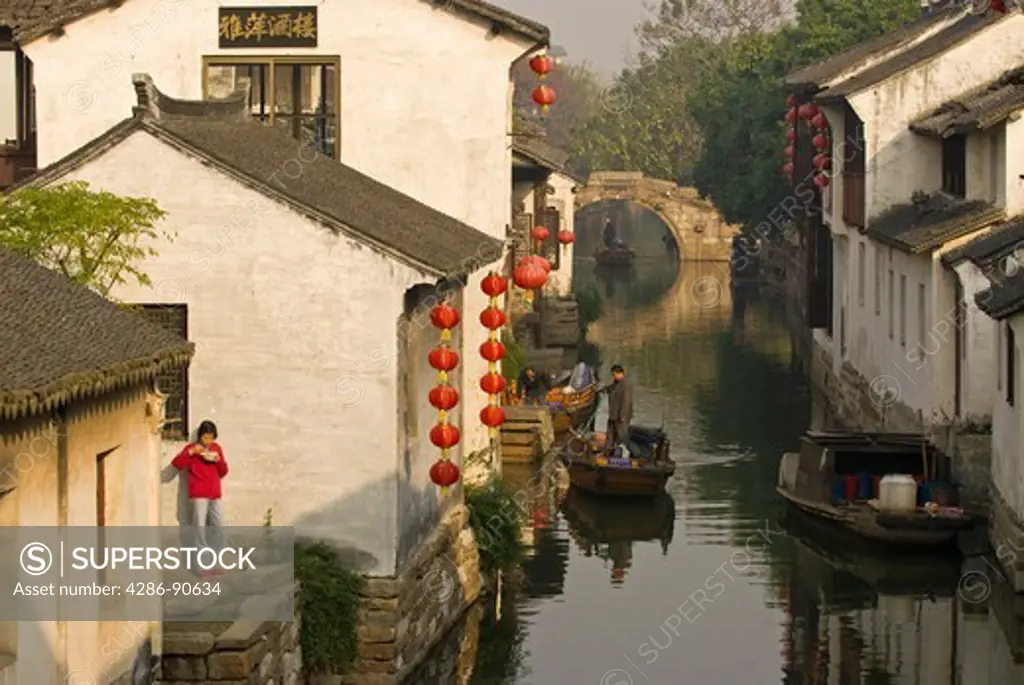 Woman eats early morning rice as row boats travel canal of historic water town, Zhouzhuang, Jiangsu Province, China