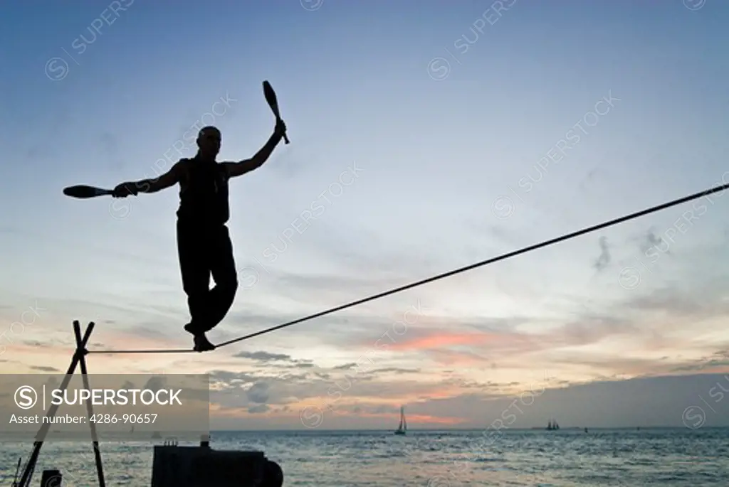 Tight rope walker juggles over ocean at sunset, Mallory Square, Key West, Florida