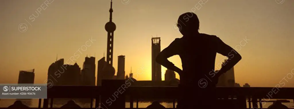 Sunrises over skyline as elderly man exercises tai chi, The Bund, Shanghai, China