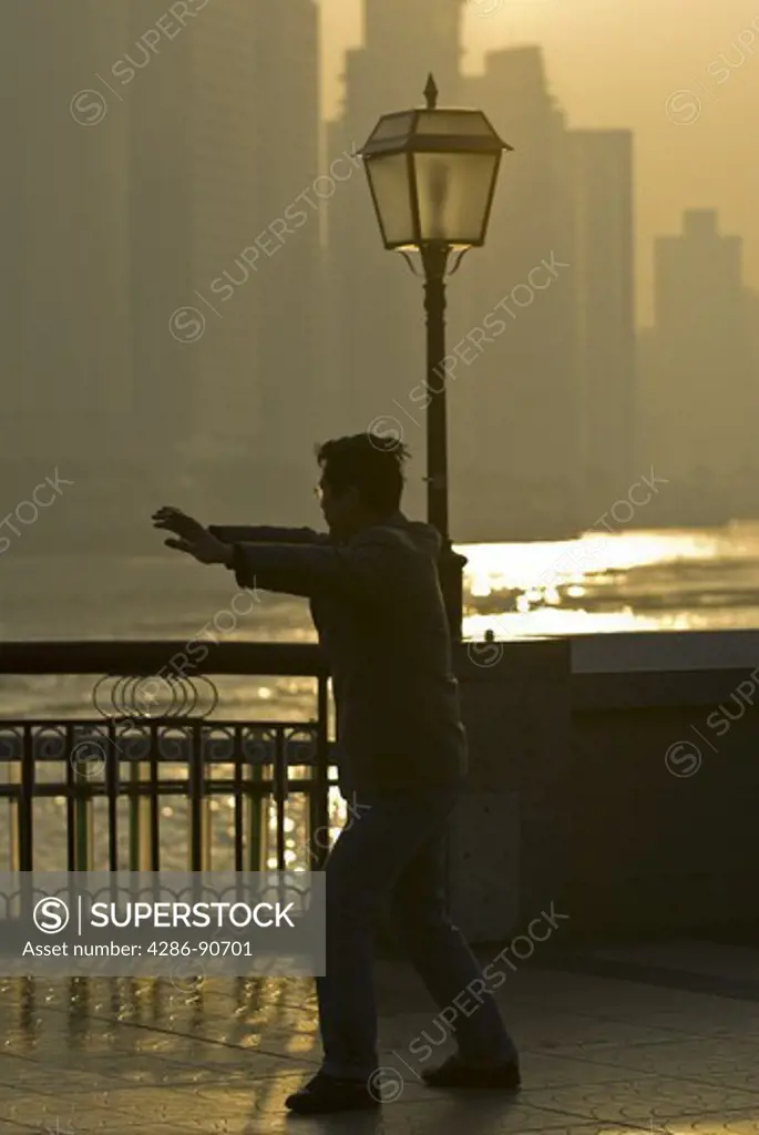 Sunrises over skyline as man exercises tai chi, The Bund, Shanghai, China