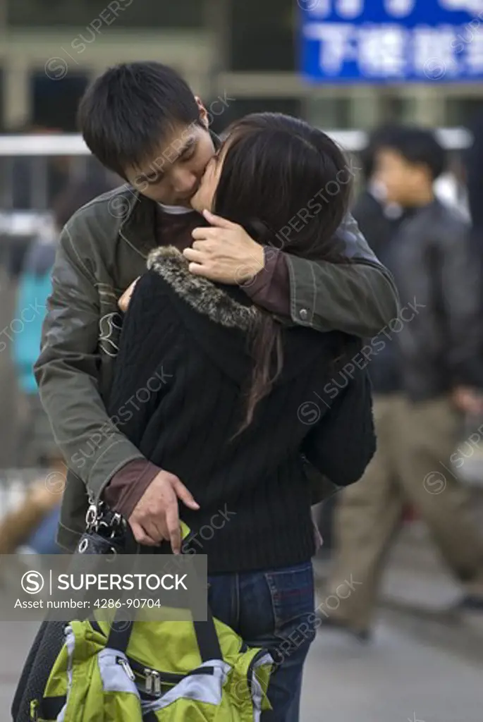 Young boyfreind and girlfriend kiss in busy train station, Shanghai, China