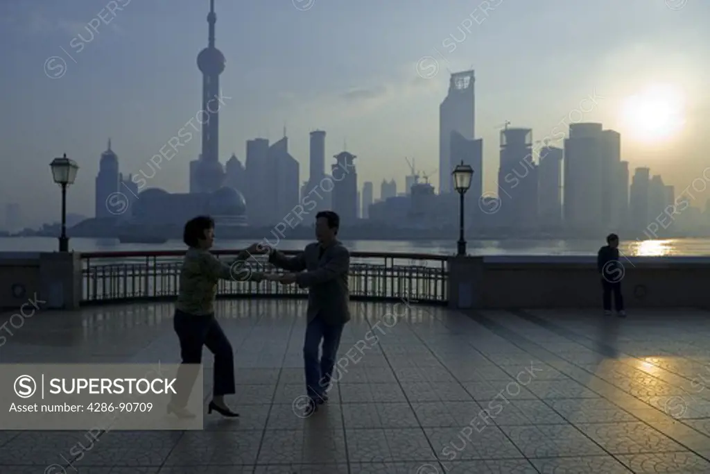 Couple dances for exercise as sun rises over skyline, The Bund, Shanghai, China