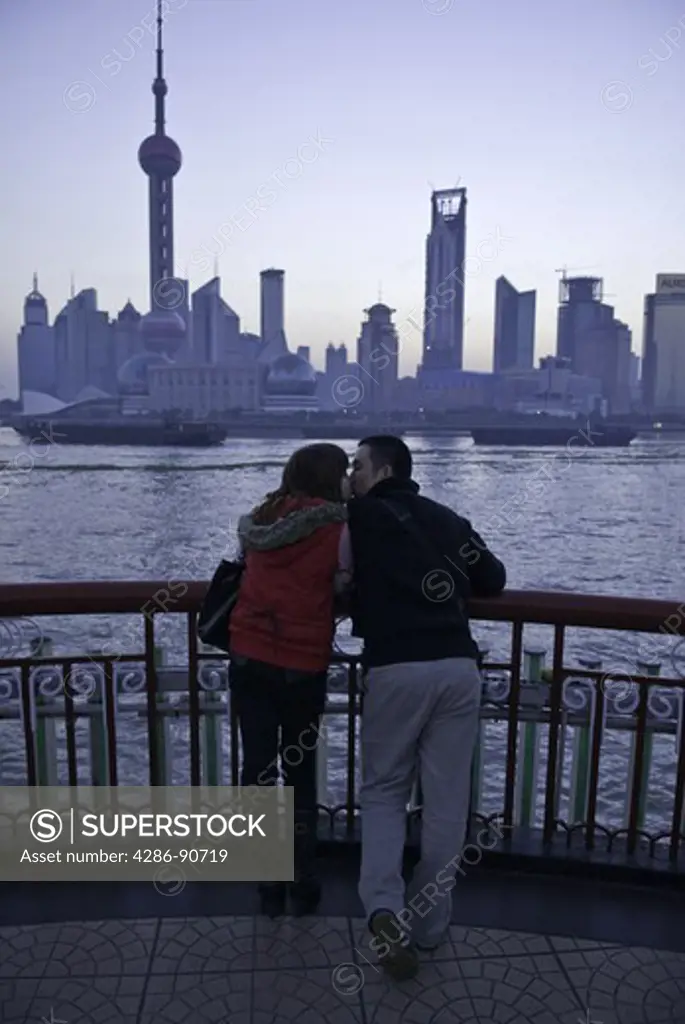 Young couple kiss and cuddle before dawn along skyline, The Bund, Shanghai, China