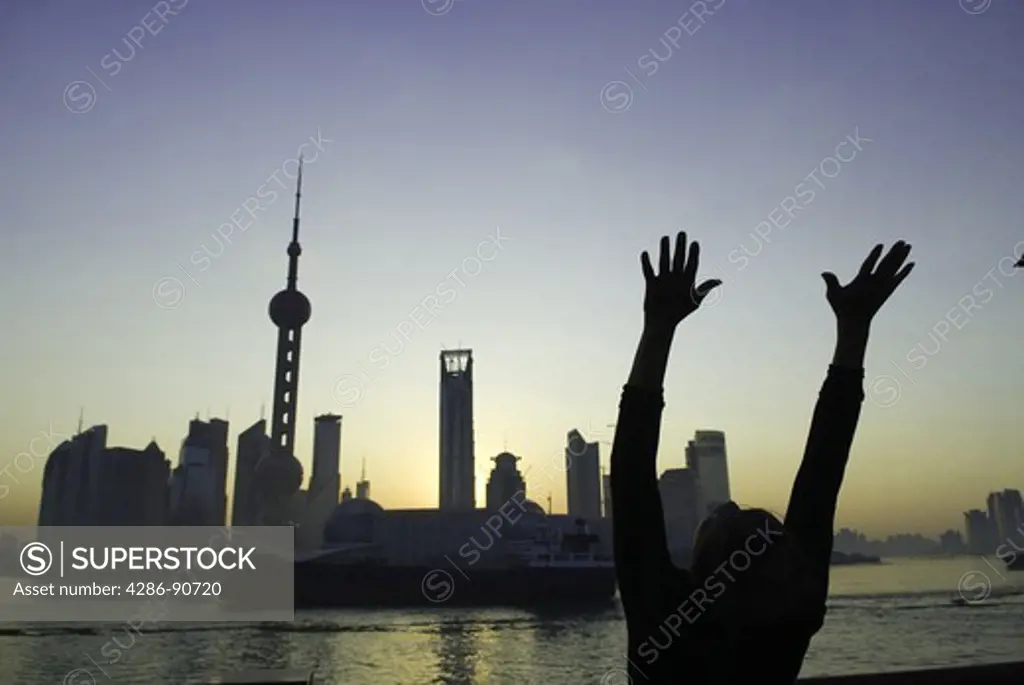 Sunrises over skyline as elderly man exercises tai chi, The Bund, Shanghai, China