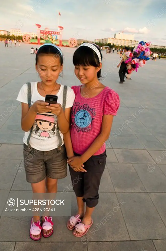 Westernized teen girls send text messages on cellular telephone, Xiwuzhumuqinqi, Inner Mongolia, China