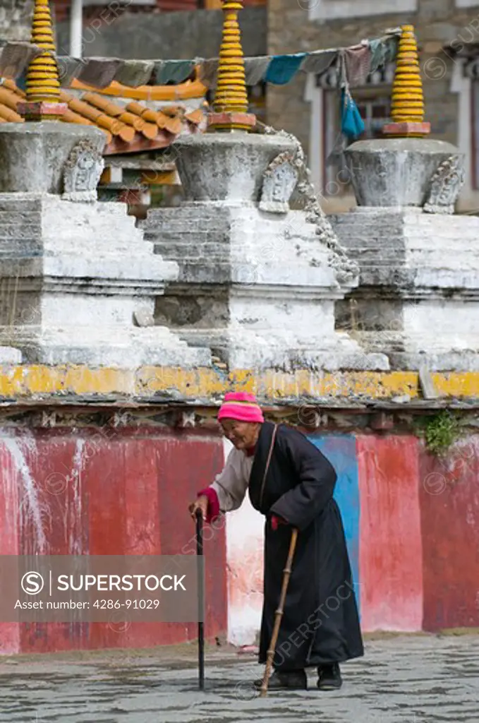Elderly Tibetan Buddhist pilgrim with canes circumambulates Tagong Monastery, Sichuan Province, China