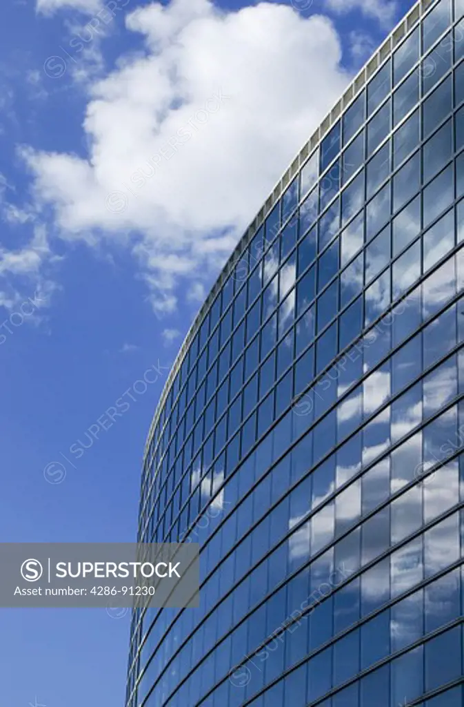 White clouds and a blue sky reflecting in the mirrored windows of a modern building.