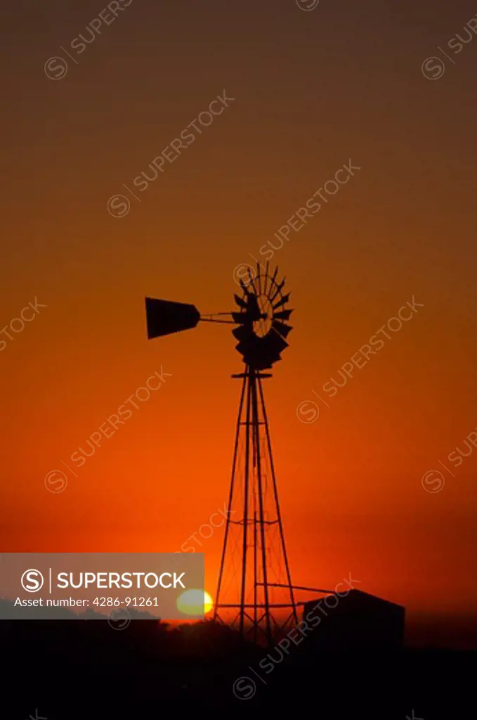 Silhouette of water pumping windmill with sun in background in Western United States.