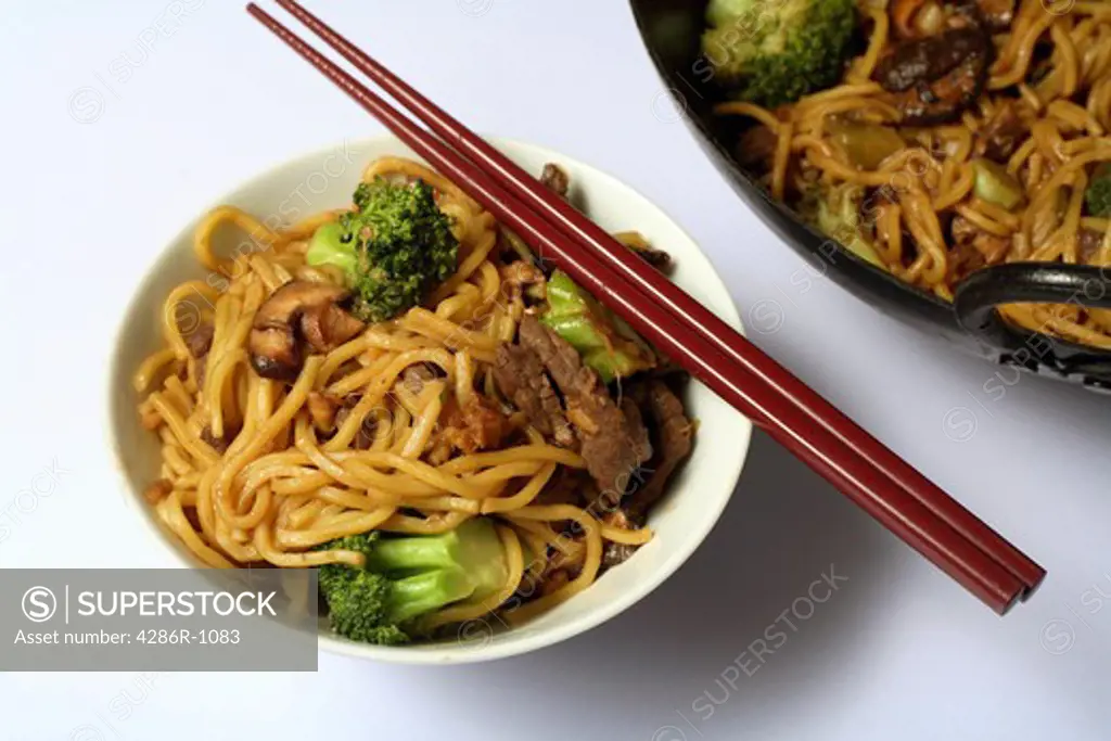 Beef chow mein and a chopsticks from above, with part of the wok in the background.  beef; chow; mein; fork; noodles; egg noodles; wok; chow mein; beef chow mein; chinese; meal; food; dinner; broccoli; brocolli; cooking; cooked; close-up