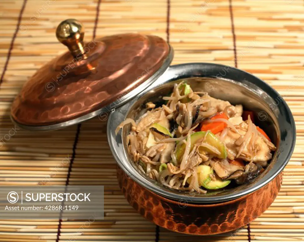 Chinese stir-fried chicken with vegetables in an oriental serving bowl on a traditional mat.