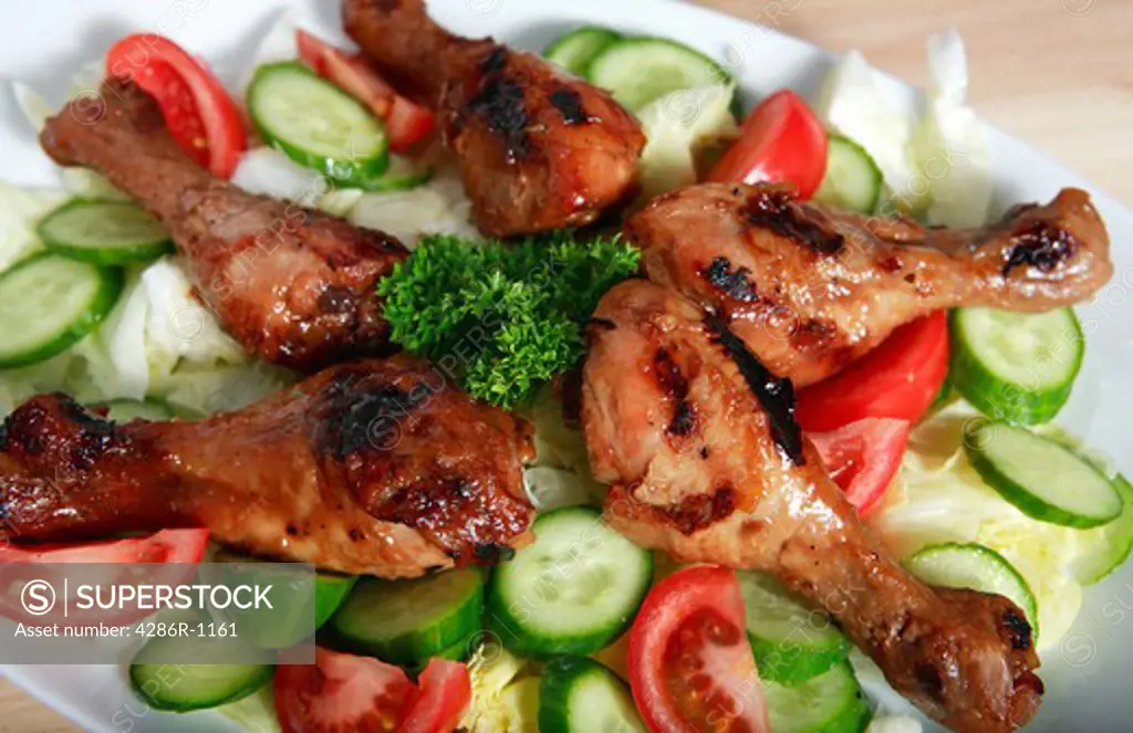 A plate of chinese-style marinade-glazed grilled chicken drumsticks served with a salad.
