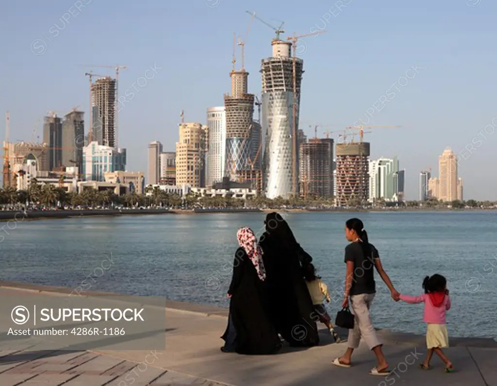 Covered Qatari women with their children and housemaid strolling on the Corniche in Doha, Spring 2008, with the New District construction work taking place across the Doha Bay.